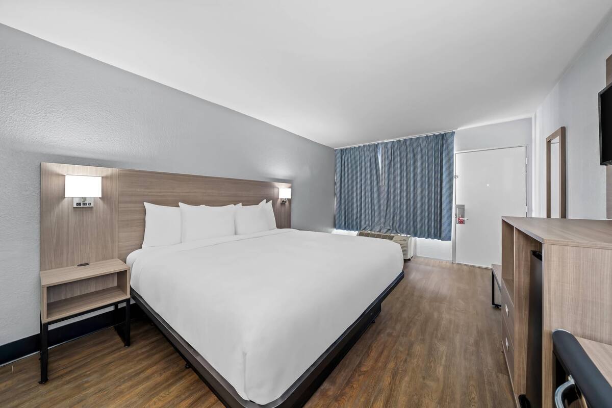 Ein modernes Hotelzimmer mit einem großen Bett, Nachttischen, einem Schreibtisch und einem Fernseher.