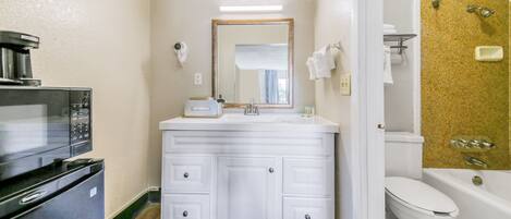 A compact bathroom with a white vanity, a sink, a mirror, a toilet, and a shower area.