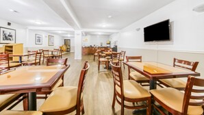 A dining area with wooden tables and chairs, a flat-screen TV mounted on the wall, and framed pictures on the walls. - Econo Lodge Daytona Beach - Speedway (Daytona Beach)