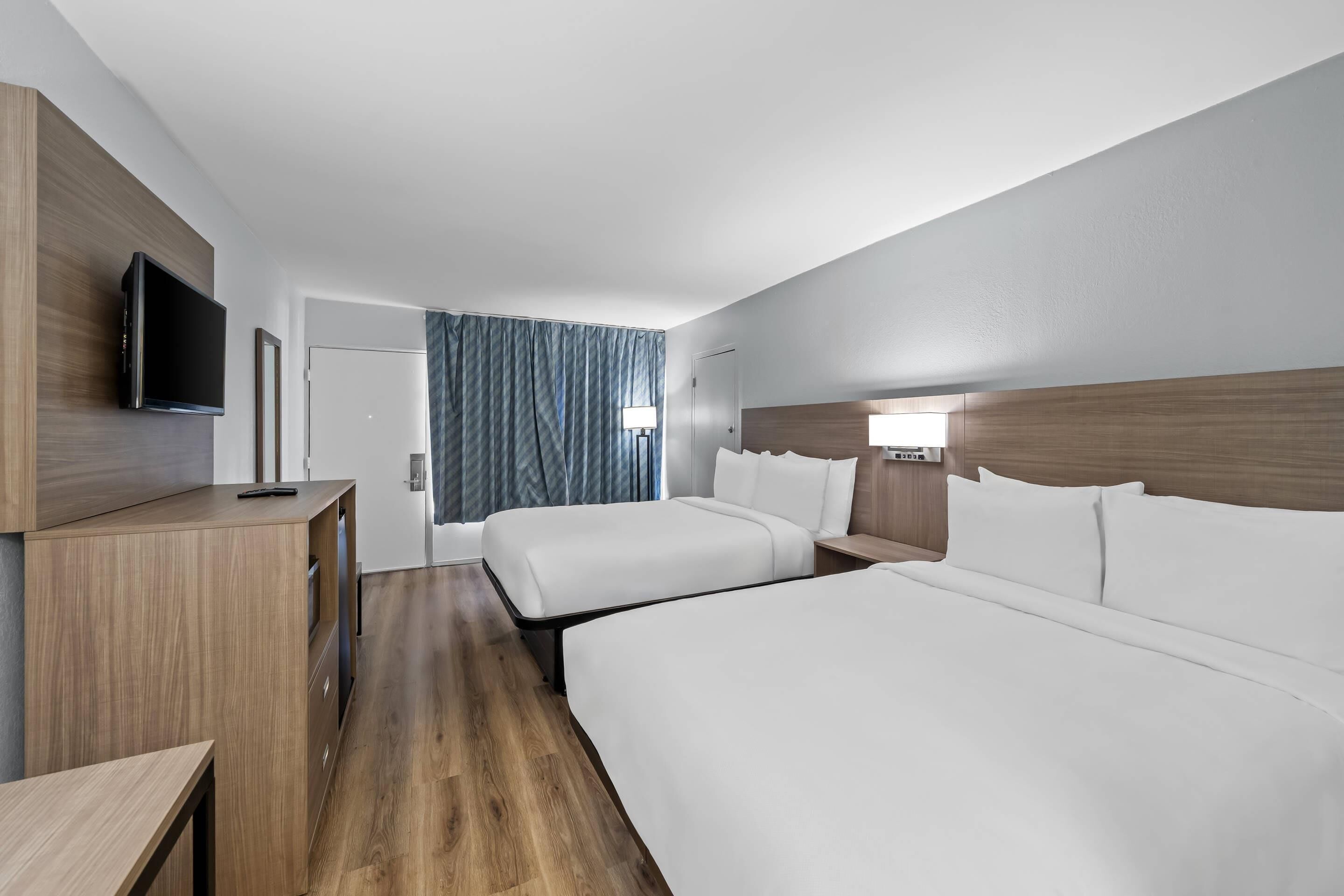 Een hotelkamer met twee bedden, een televisie, een bureau en een raam met gordijnen.