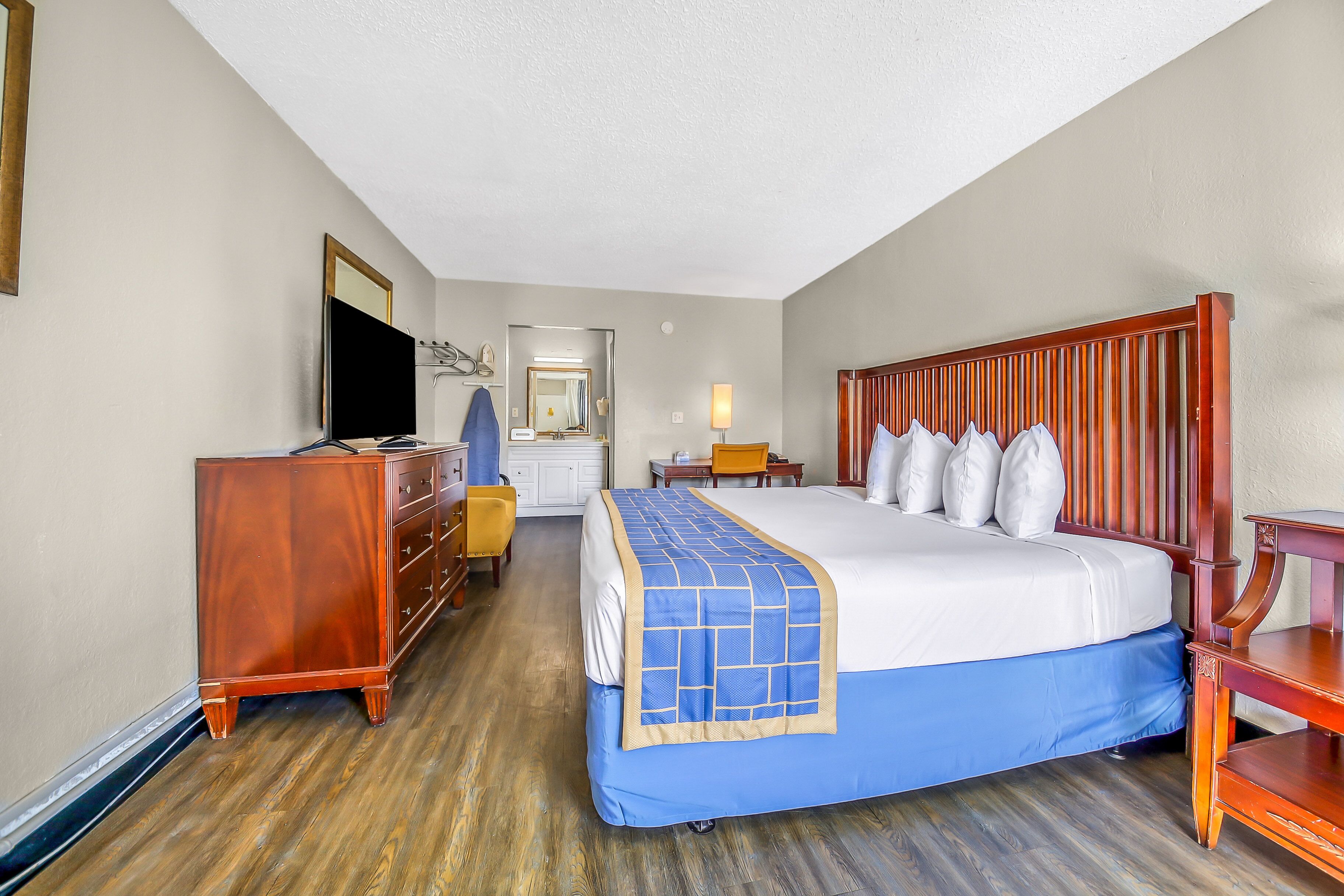 A hotel room with a large bed, a dresser, a television, and a desk with a chair.
