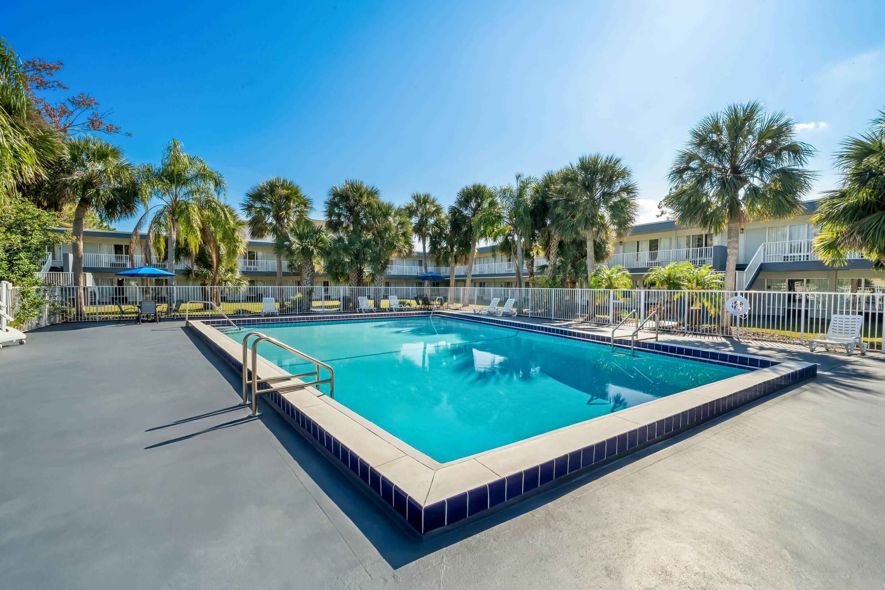 A rectangular pool with a tiled edge, surrounded by a white fence and palm trees.