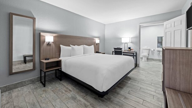 A modern hotel room with a large bed, bedside tables, a mirror, and a bathroom visible through an open door. - Econo Lodge Daytona Beach - Speedway (Daytona Beach)