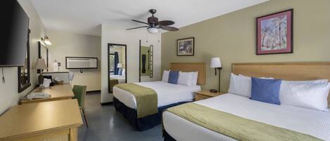 A hotel room with two beds, a desk, a chair, a ceiling fan, and a painting on the wall.