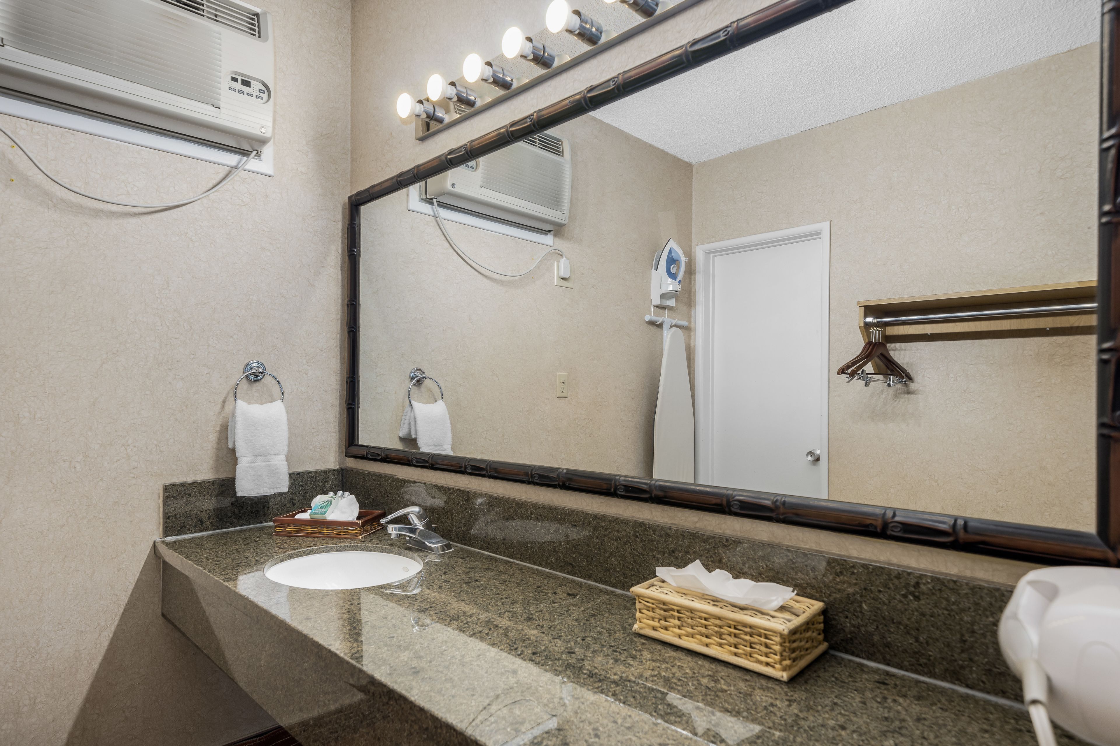 A bathroom with a granite countertop, a white sink, a mirror, a towel rack, a shower, and a hairdryer.