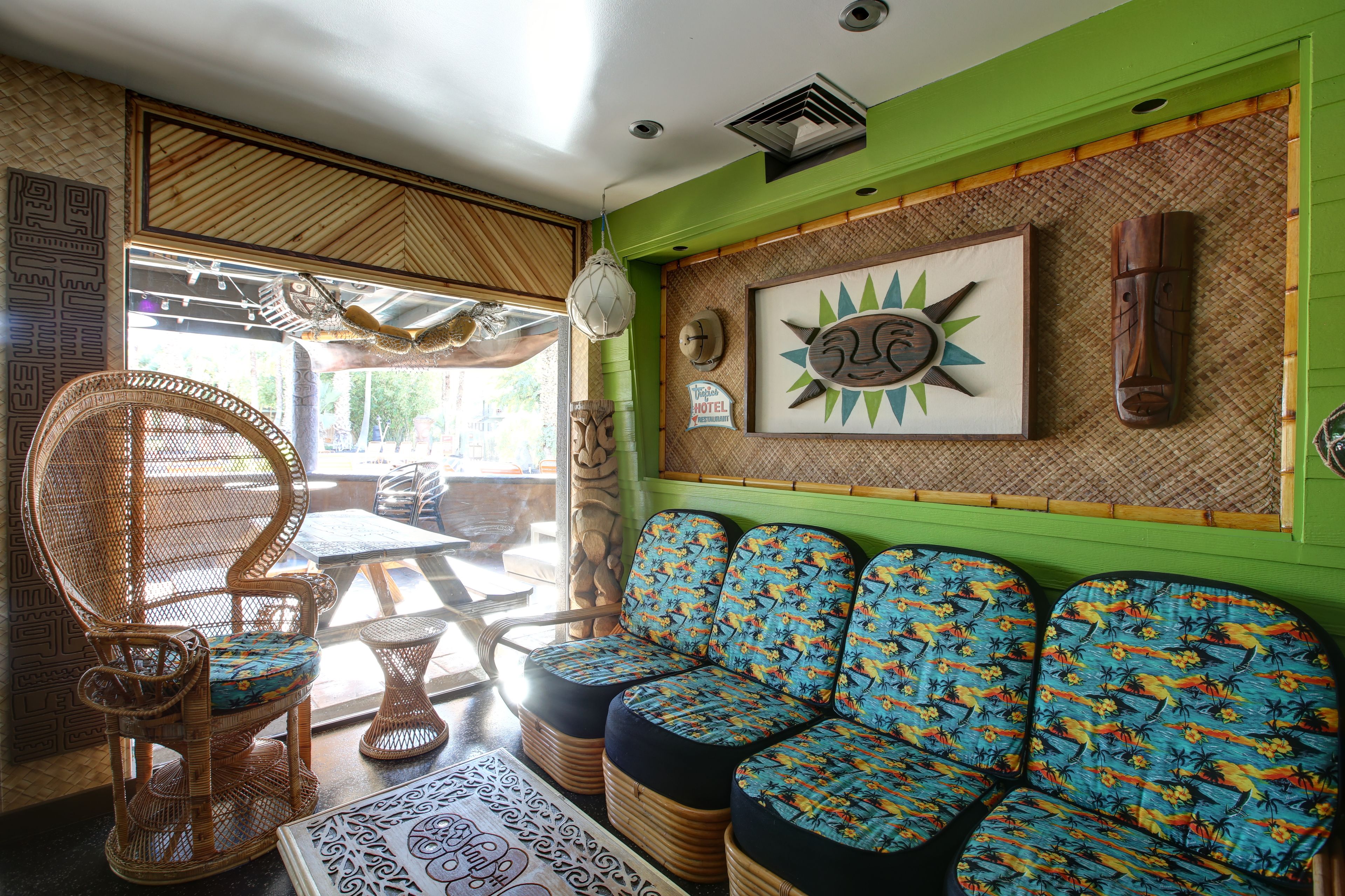 Una habitación con pared verde, muebles de mimbre y una obra de arte con forma de sol.