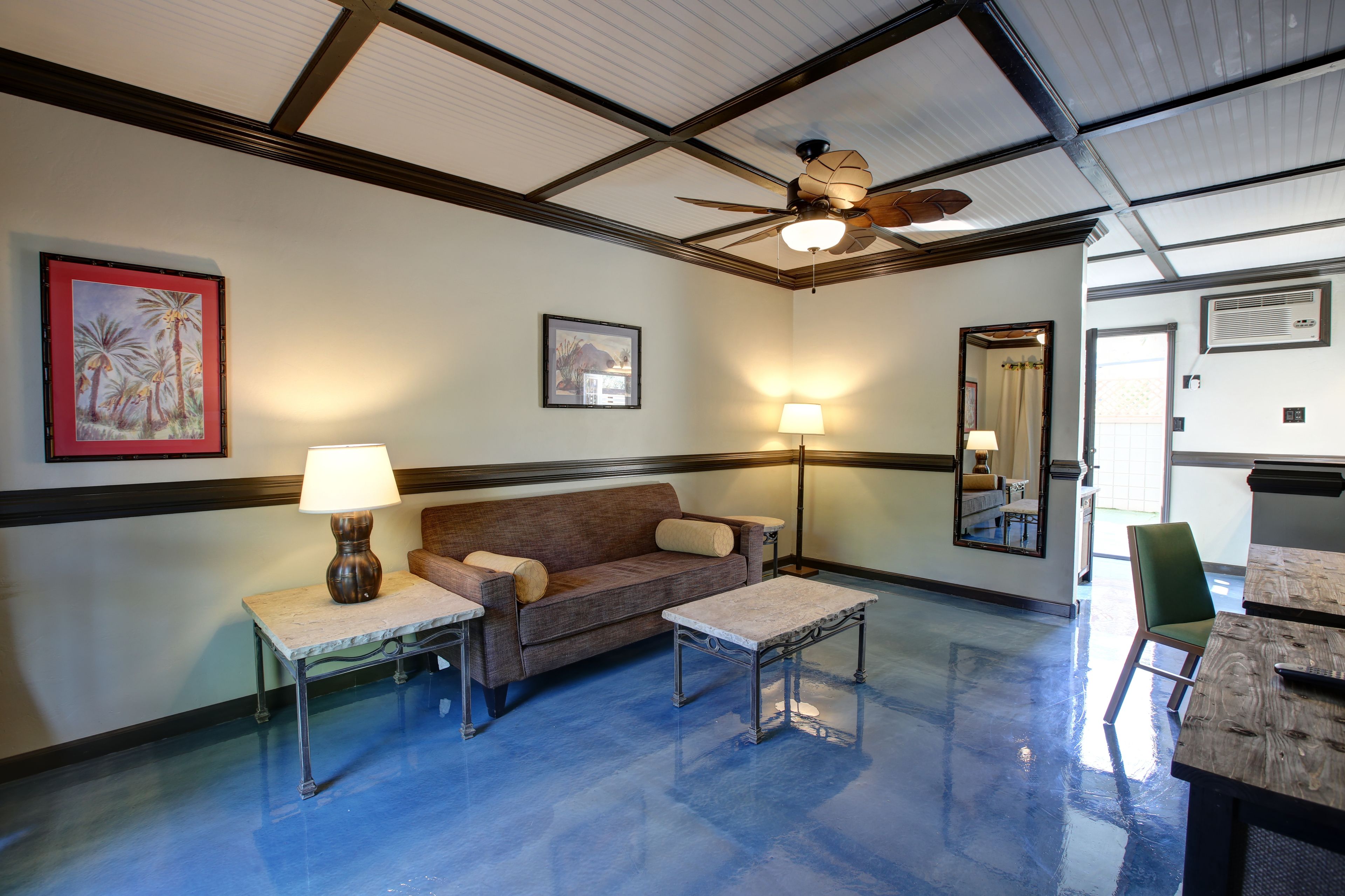 A room with a ceiling fan, a sofa, two tables, and a chair.