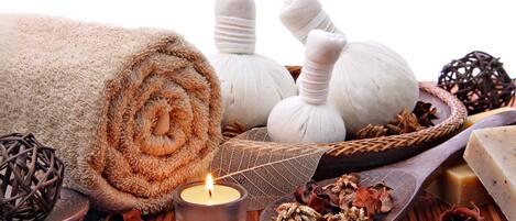 A spa setting with a rolled towel, candles, and massage stones.