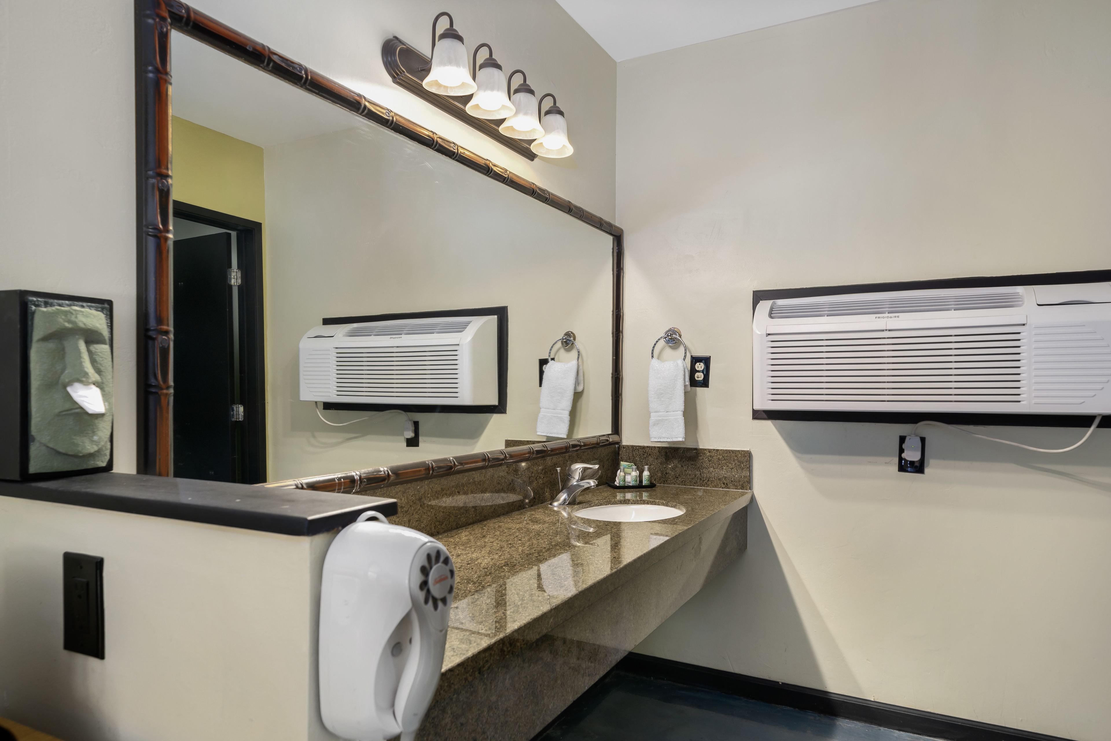 Un baño con encimera de granito, un espejo grande, aire acondicionado de pared y un secador de manos.