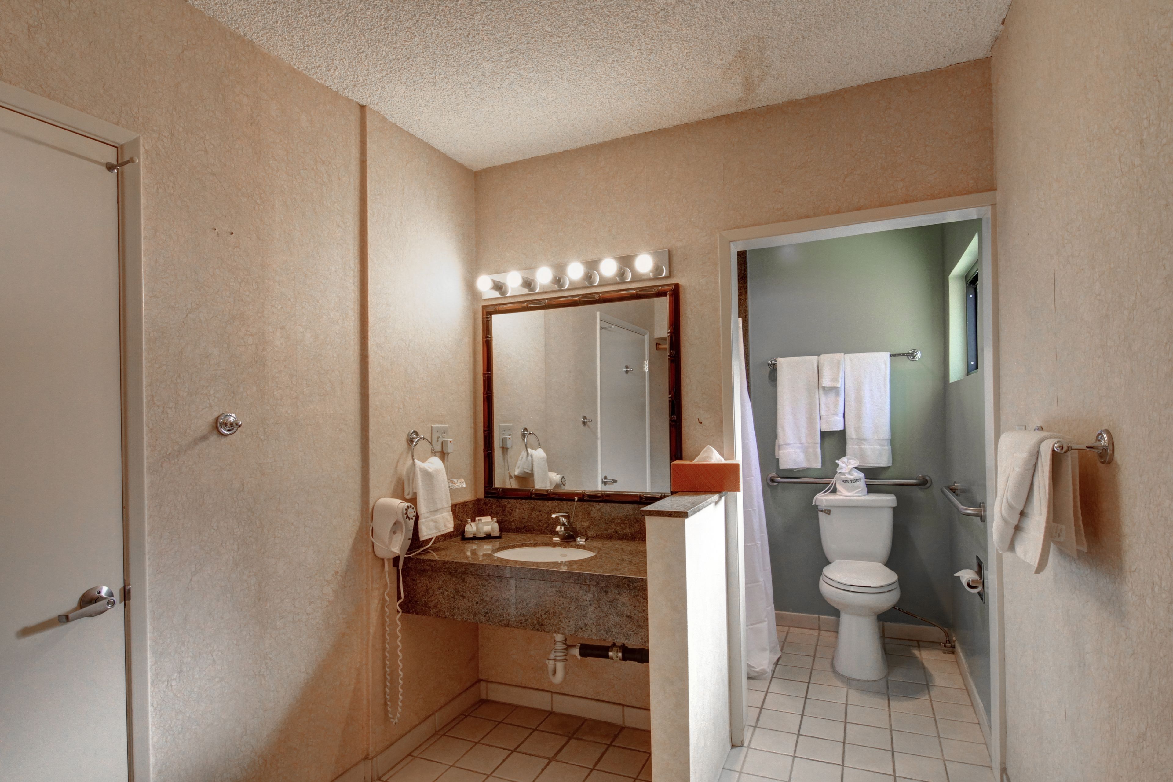 Un baño con tocador, lavabo, espejo con iluminación, inodoro y zona de ducha.