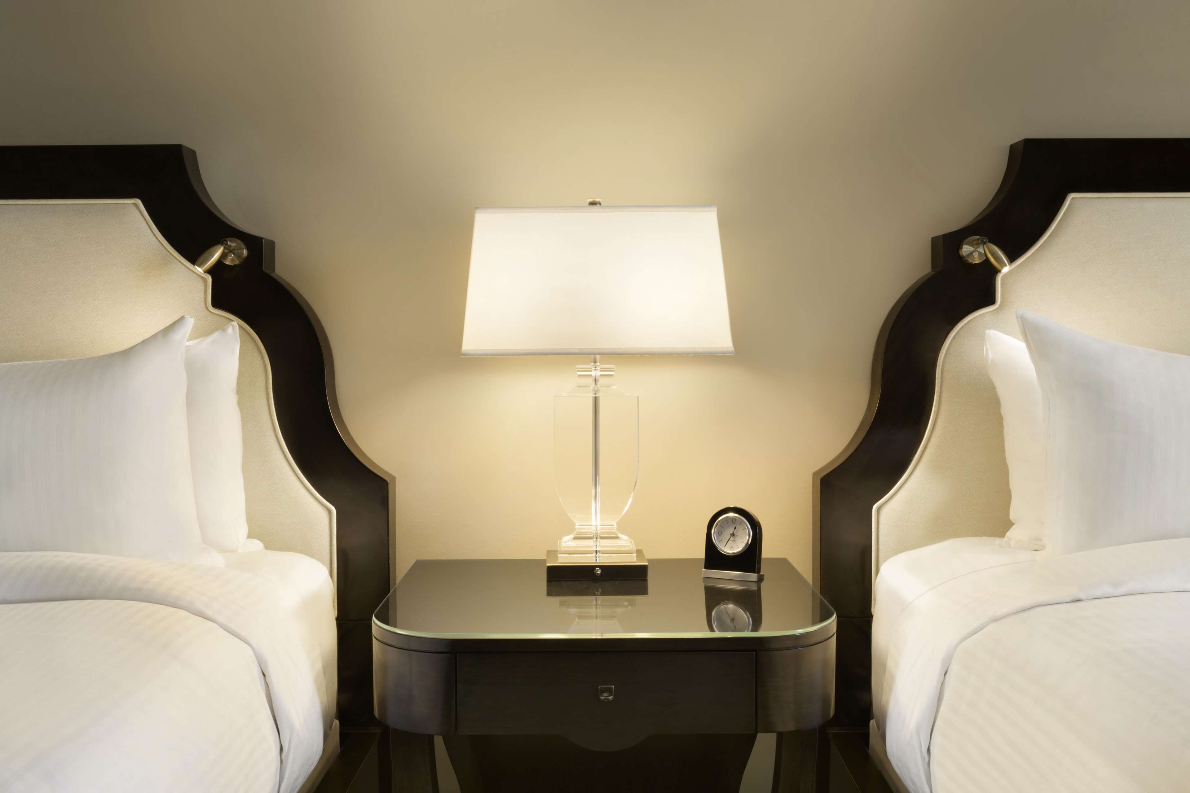 A hotel room with two beds, a nightstand with a lamp, and a clock.