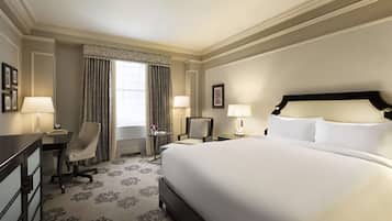 A hotel room with a large bed, two bedside tables with lamps, a desk with a chair, and a window with curtains.