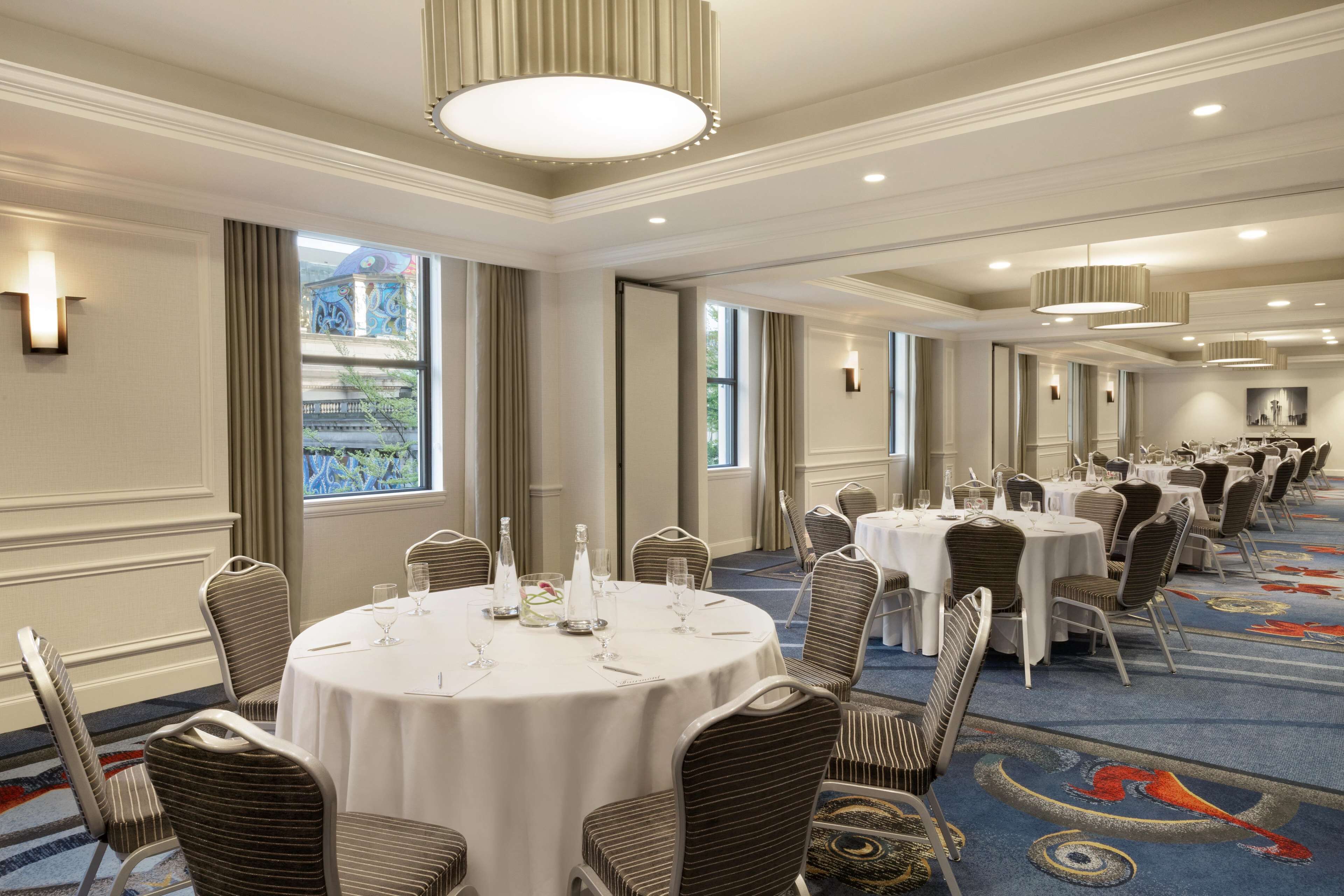 A hotel conference room with round tables, chairs, and a carpeted floor.