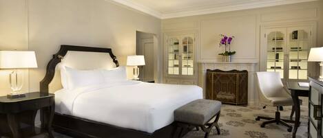 A hotel room with a large bed, two bedside tables with lamps, a chair, a desk, and a chandelier.