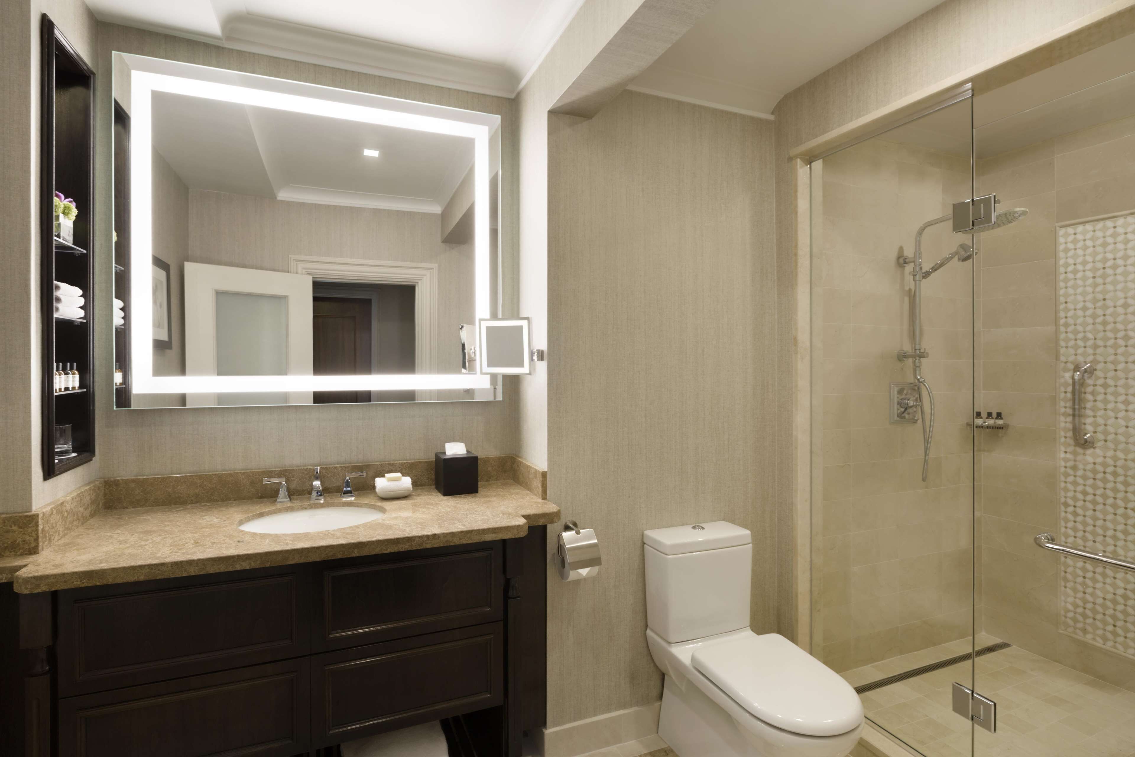 A bathroom with a large mirror, a sink, a toilet, and a glass-enclosed shower.
