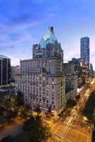 Um edifício grande e histórico com uma torre imponente e vários andares, rodeado por edifícios modernos e altos.