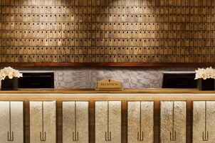 Una zona de recepción con un muro de madera que exhibe numerosas cartas, un mostrador de recepción y dos arreglos florales.