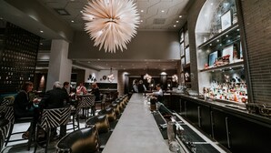 Zona de bar moderna con una barra larga, asientos a ambos lados y una lámpara de techo distintiva.