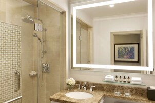 Un baño moderno con ducha envuelta en vidrio, lavamanos de mármol y un espejo grande.