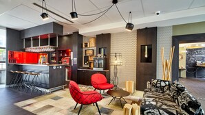 A modern interior with a bar area, red chairs, a patterned sofa, and a patterned wall.