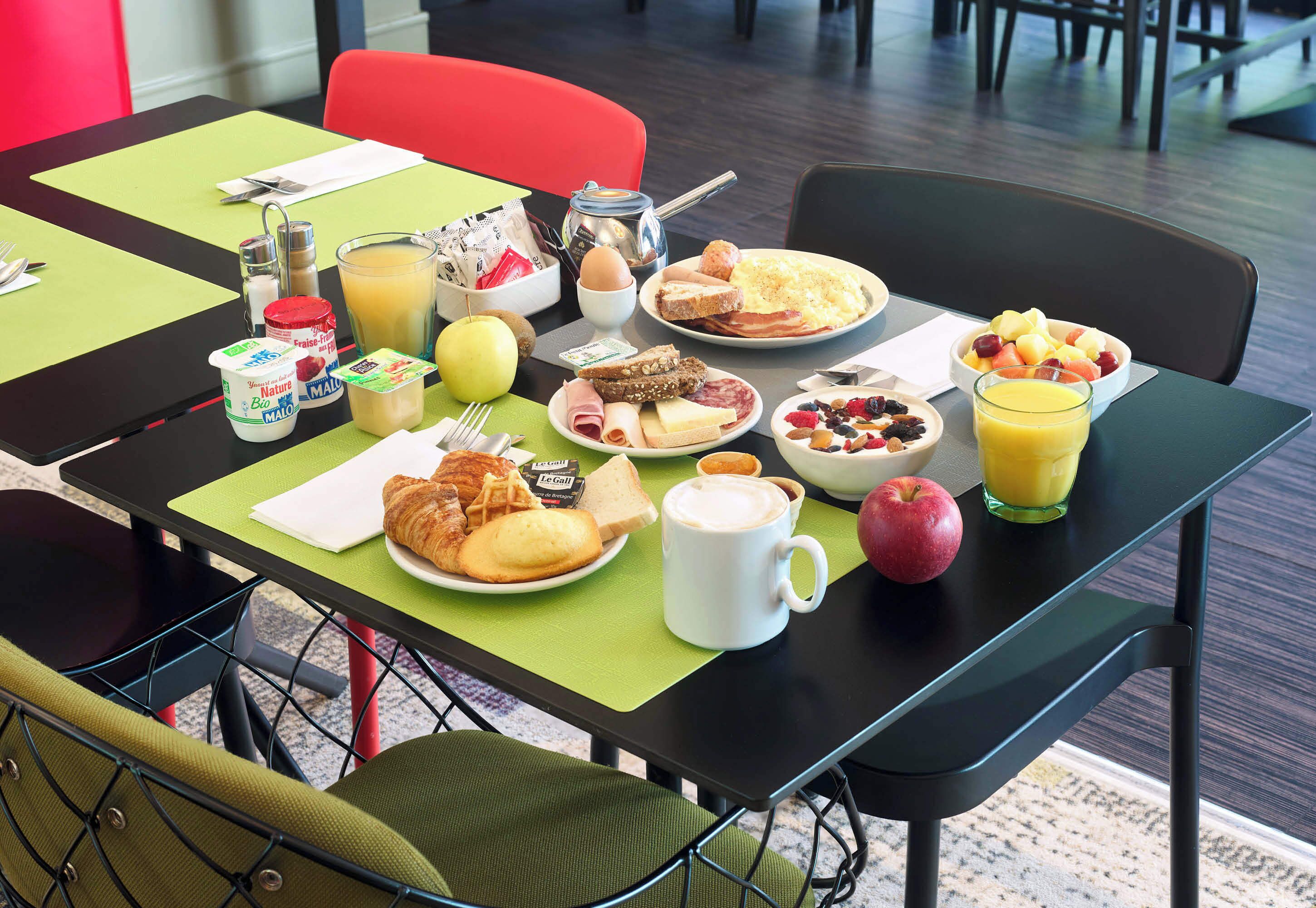 Una mesa de desayuno con diferentes alimentos, una taza de café y un vaso de jugo de naranja.