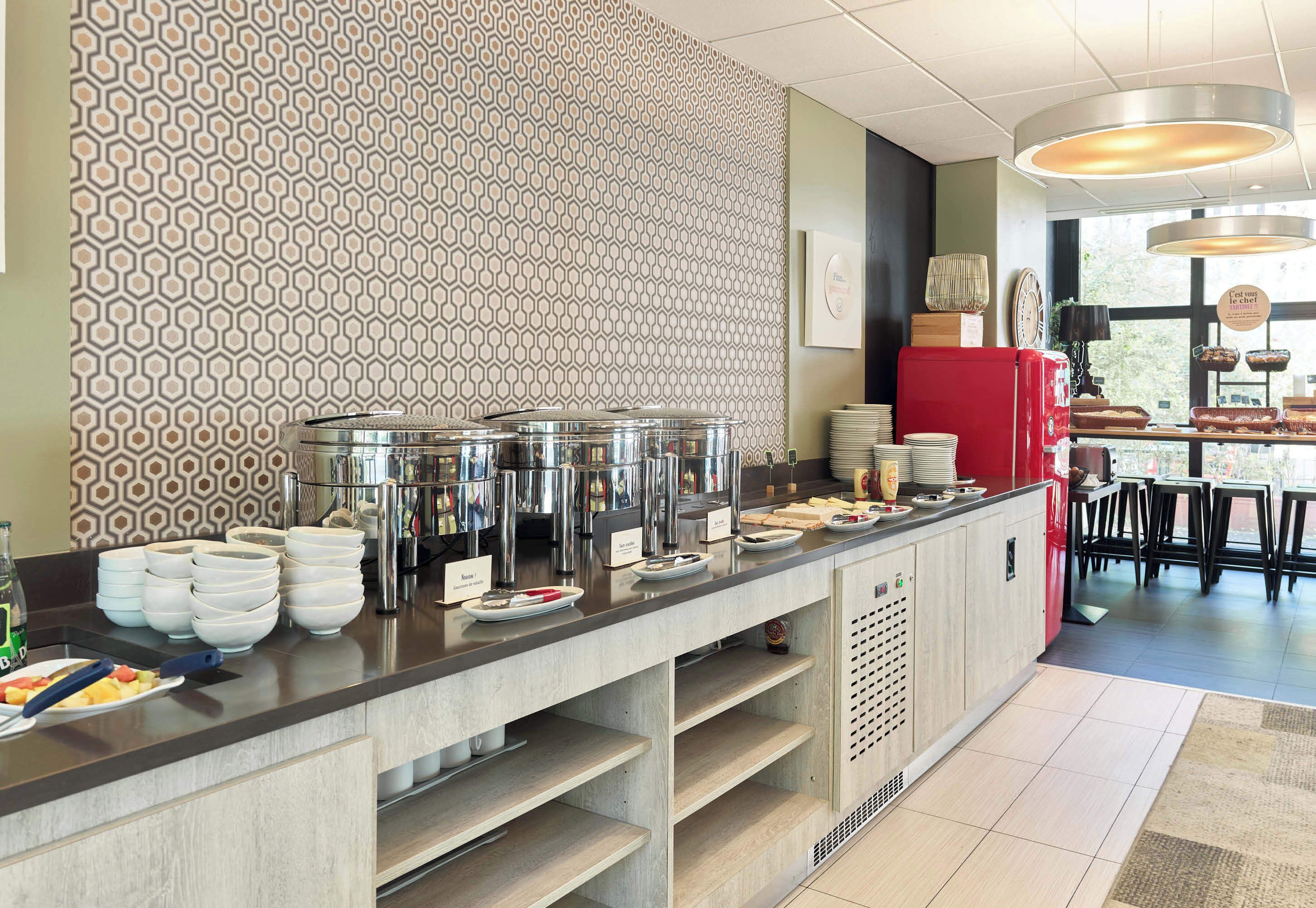 Un buffet avec plusieurs points de service, un mur décoré de motifs et un espace détente visible au fond.