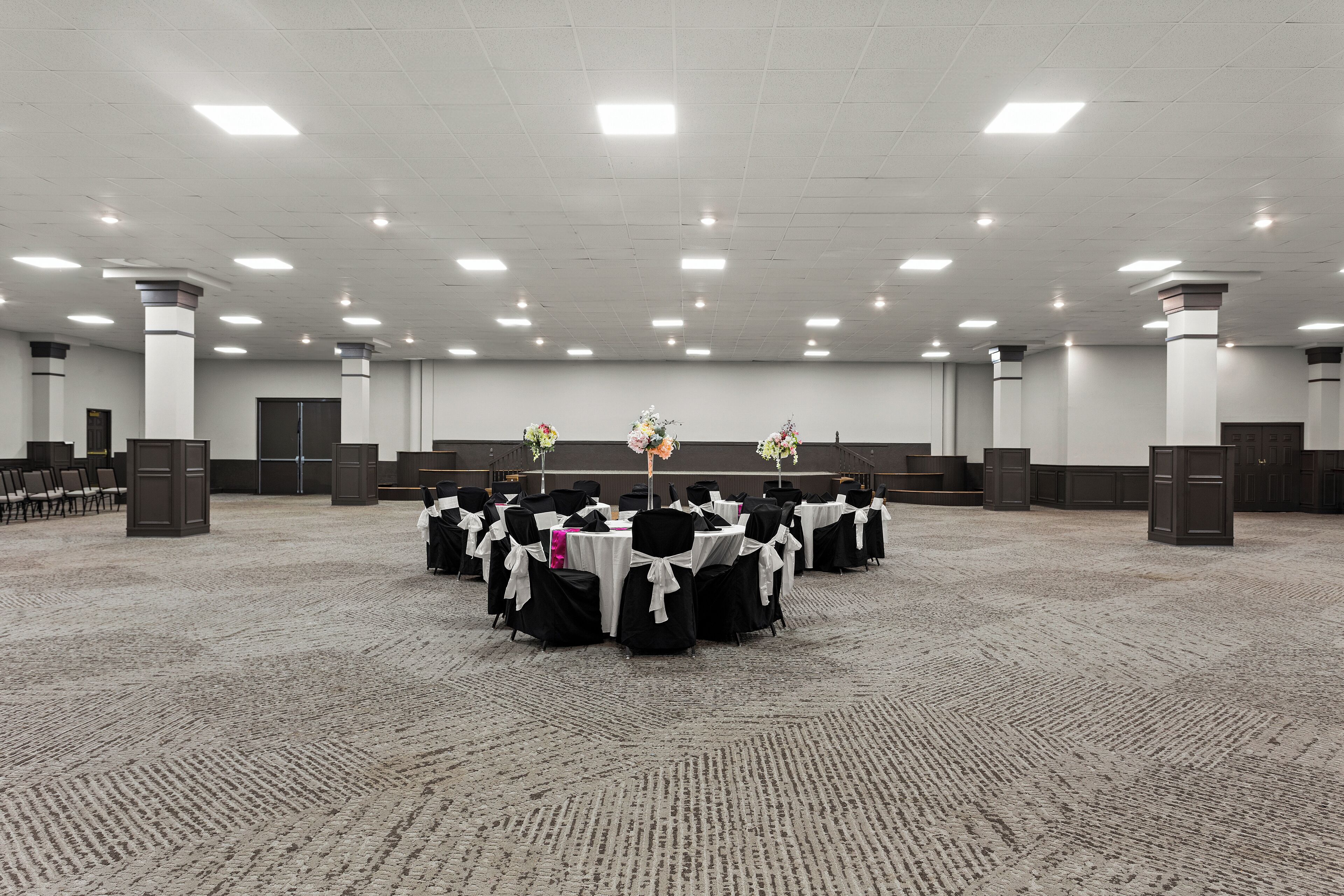 A large, well-lit conference room with round tables, black chairs, and white tablecloths.