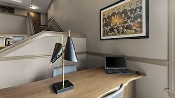 Une chambre d’hôtel moderne avec un bureau en bois, un ordinateur portable, une lampe noire et une photo de groupe encadrée accrochée au mur.