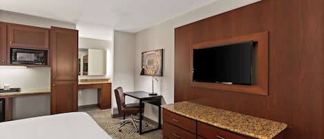 A hotel room with a bed, a desk, a microwave, a TV, and wooden cabinets.