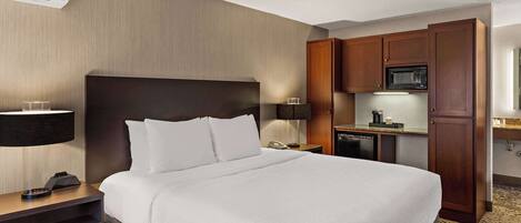 A hotel room with a large bed, a desk with a telephone and a lamp, a microwave, and a small kitchenette.