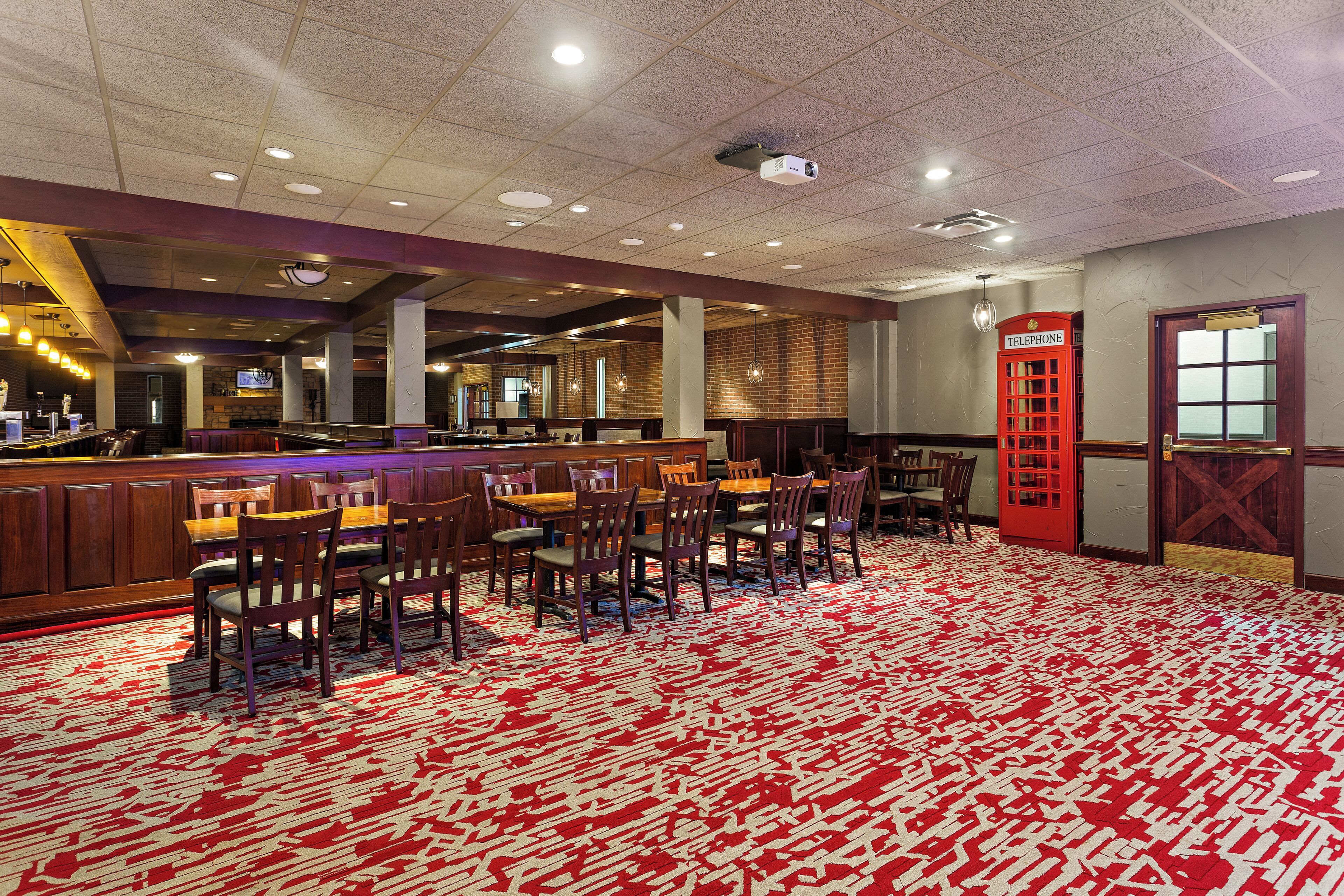 Een hotellobby met een rode telefooncel, een bar en een kamerbreed tapijt met een patroon.
