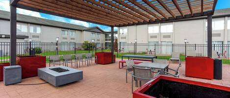 An outdoor patio area with seating, a pergola, and a view of residential buildings.