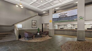 A spacious lobby with a staircase, seating area, and a large screen displaying a stadium.