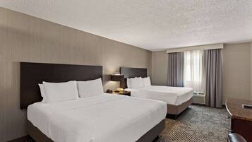 A hotel room with two beds, a desk, and a chair.