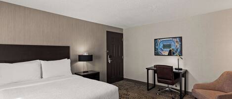 Une chambre d’hôtel avec un grand lit, un bureau avec une chaise, une porte et un tableau encadré au mur.