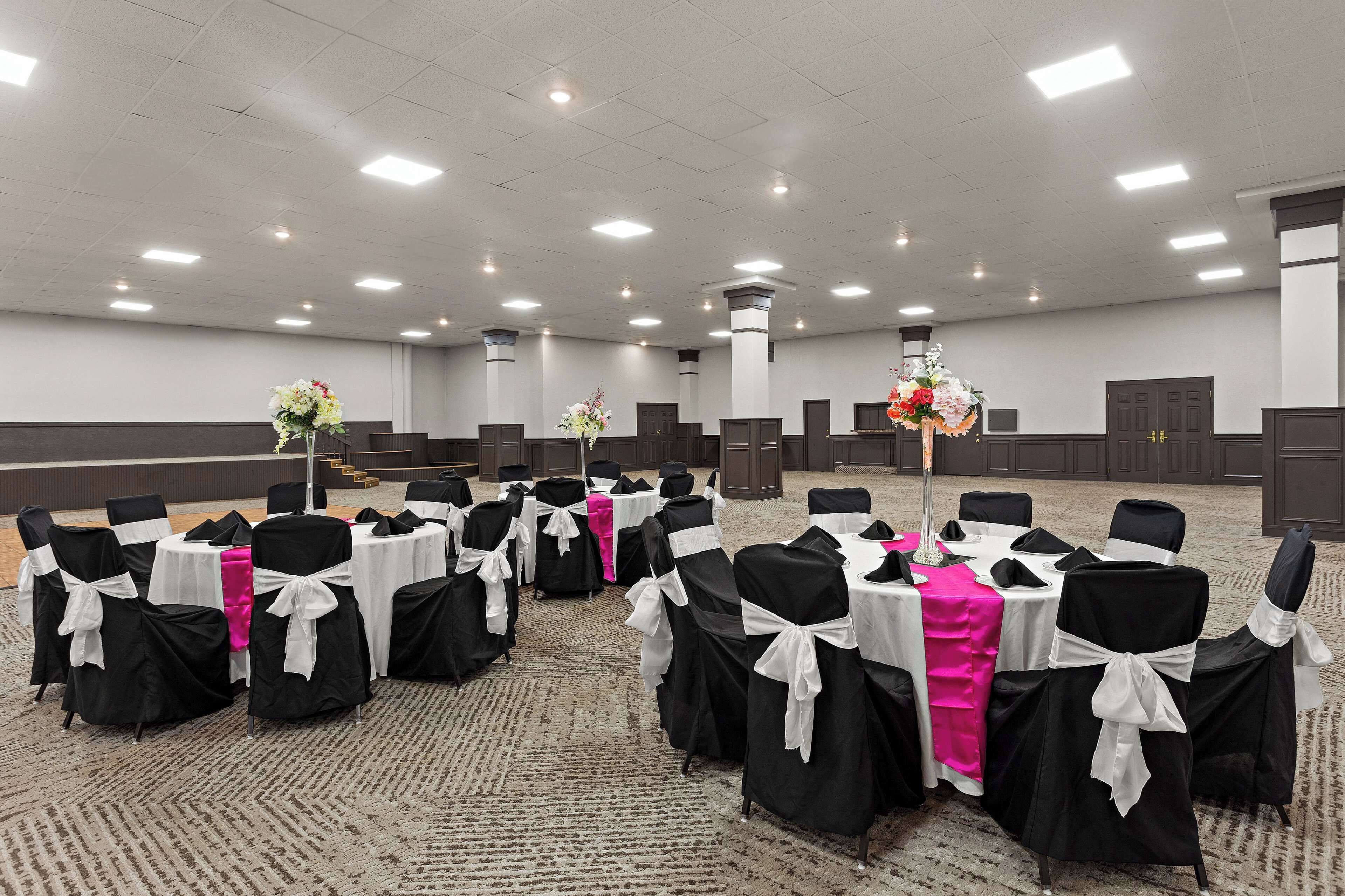 A conference room with rows of tables and chairs, each with a white tablecloth and black chair covers tied with white sashes.
