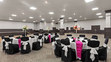 A conference room with rows of tables and chairs, each with a white tablecloth and black chair covers tied with white sashes.