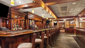 A bar area with wooden bar counters, multiple stools, and a variety of bottles.