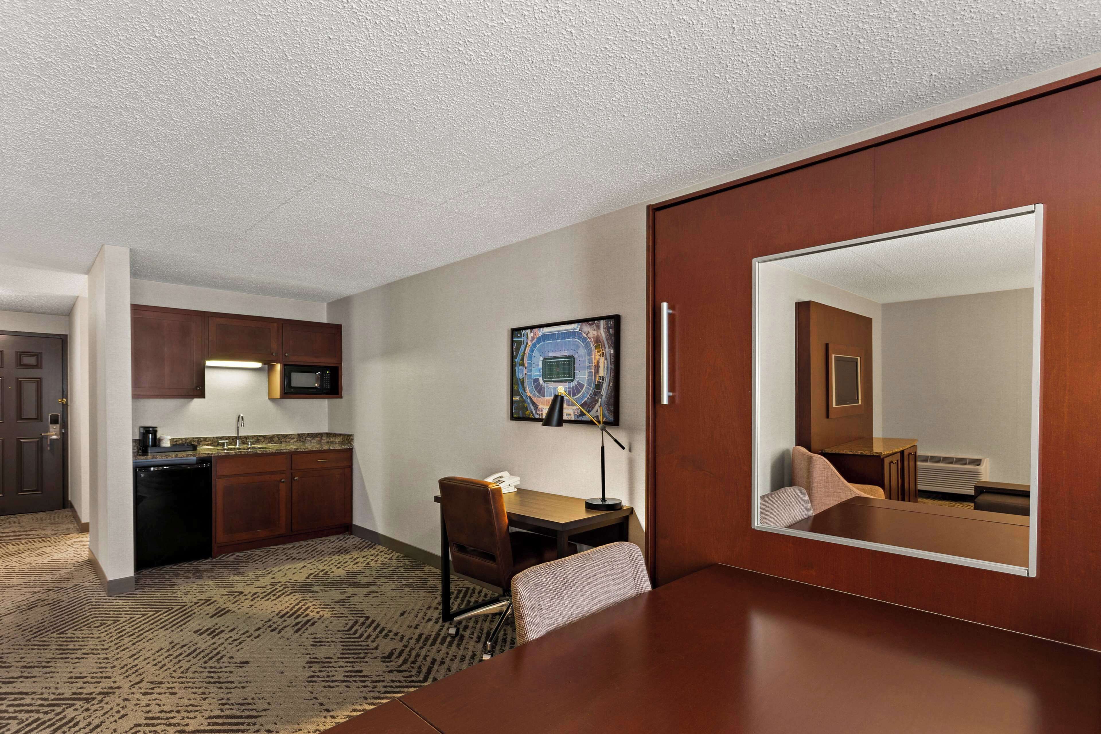 Habitación de hotel con kitchenette, zona de comedor, espejo grande y un cuadro enmarcado en la pared.