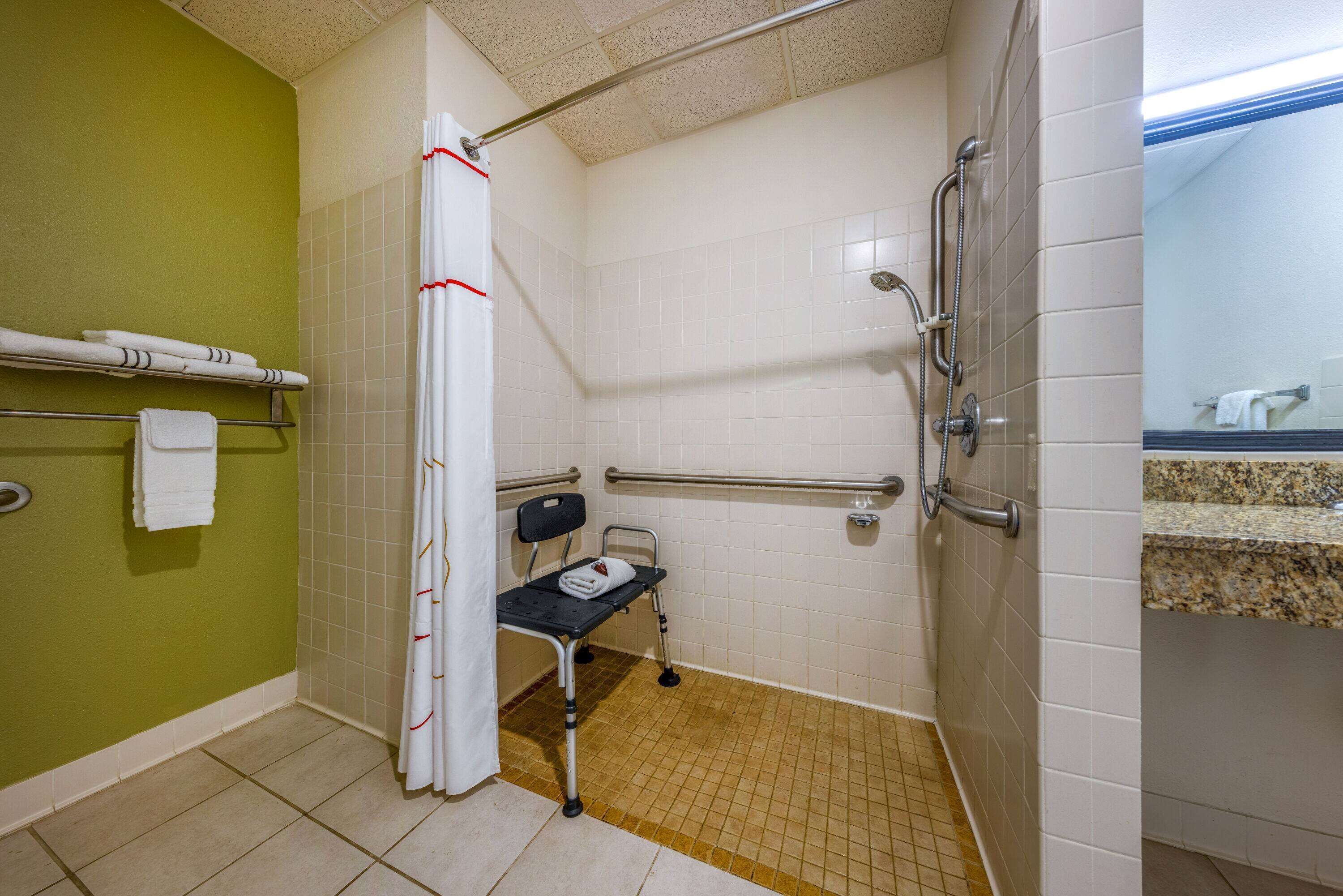 A bathroom with a wheelchair, grab bars, and a shower curtain.