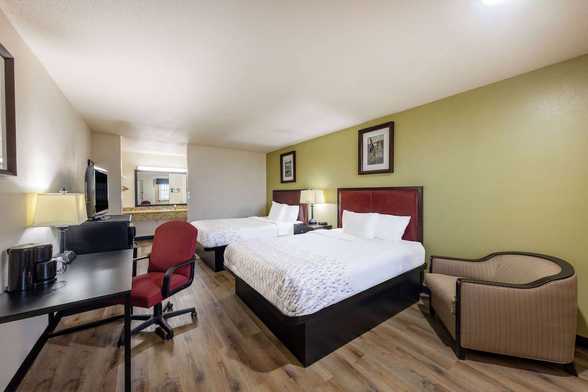 Habitación de hotel con dos camas, un escritorio con computadora, una silla y un sofá pequeño.