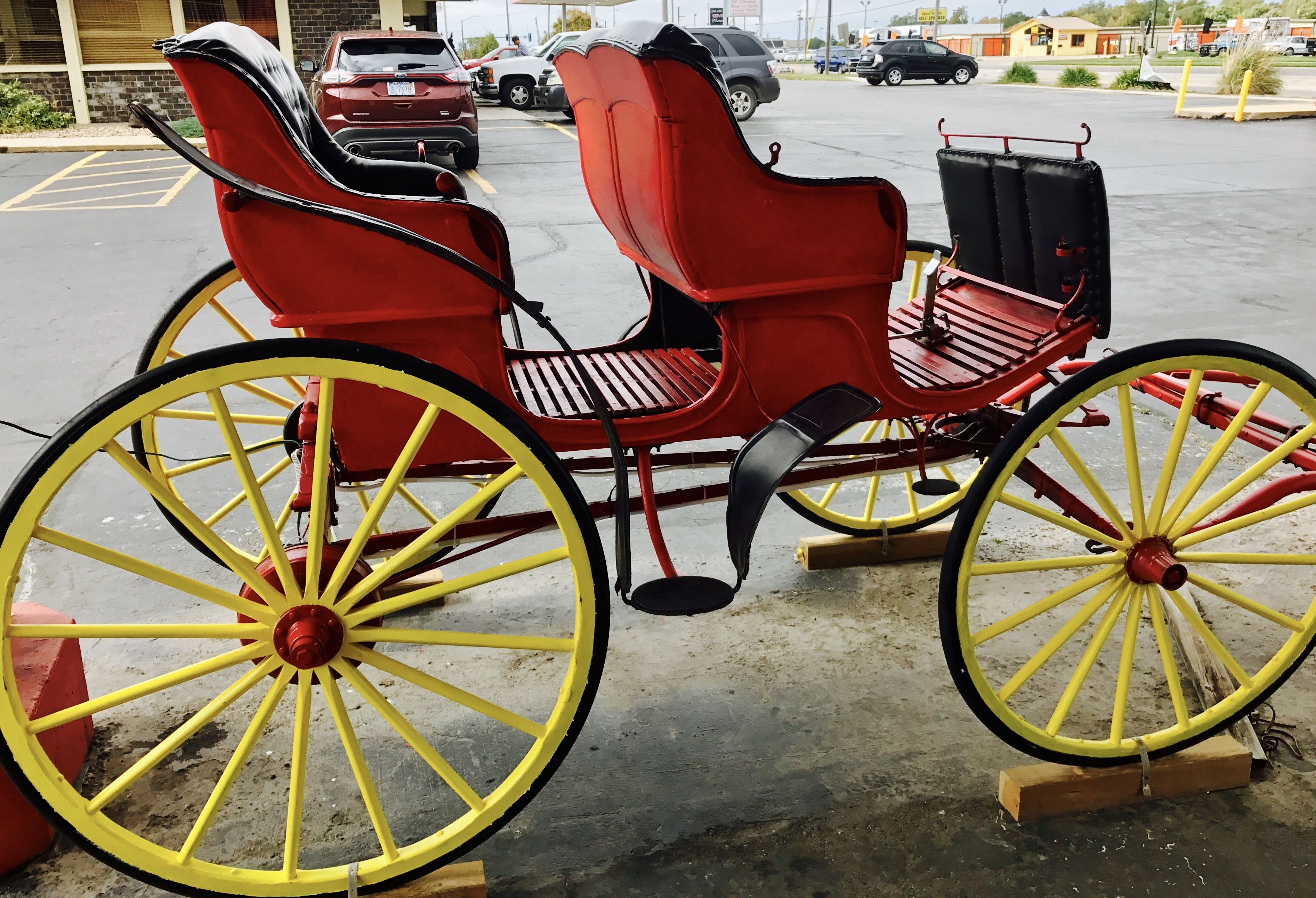 Un carruaje tirado por caballos rojo con ruedas amarillas estacionado en un estacionamiento.