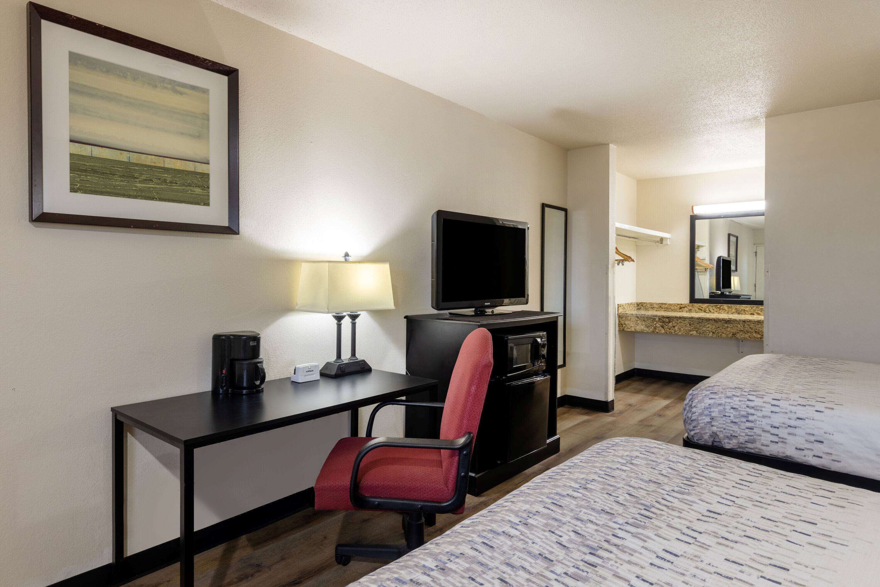 Quarto de hotel com escrivaninha, cadeira, televisão e duas camas.