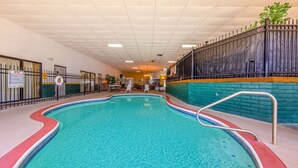 An indoor swimming pool with a tiled edge, a metal handrail, and a brick wall with a green and orange stripe. - Baymont by Wyndham El Dorado (El Dorado)