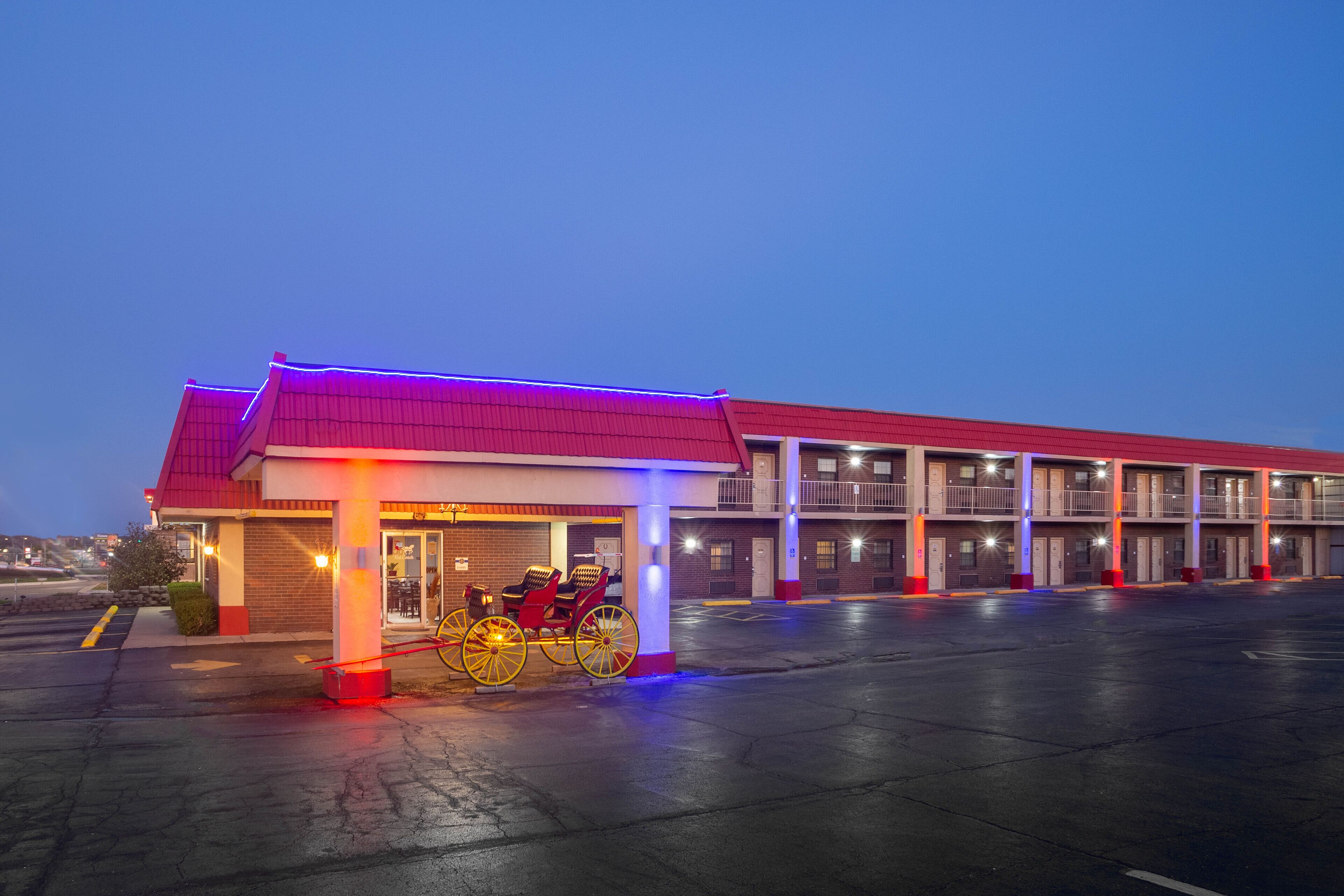 Un motel con techo rojo y varias habitaciones, un estacionamiento techado y una bicicleta estacionada afuera.