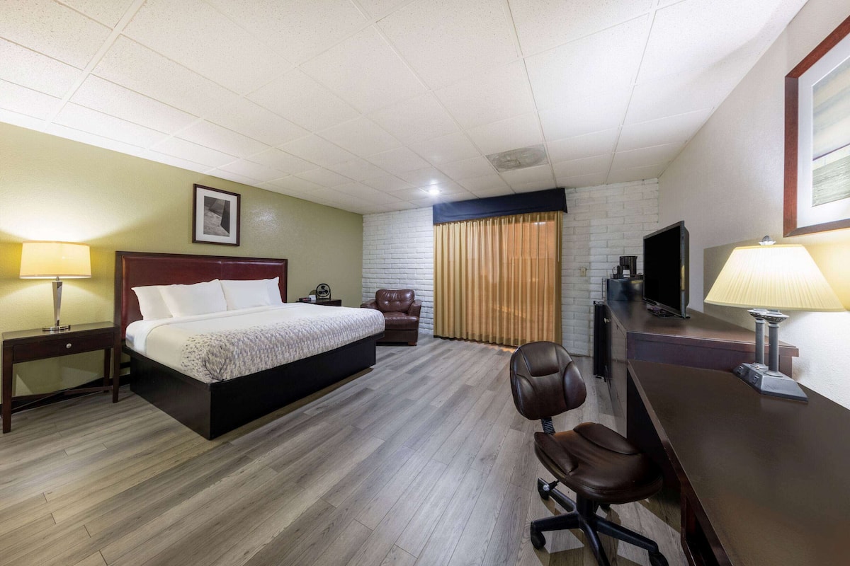Una habitación de hotel con cama, escritorio, silla, televisor y cortinas.