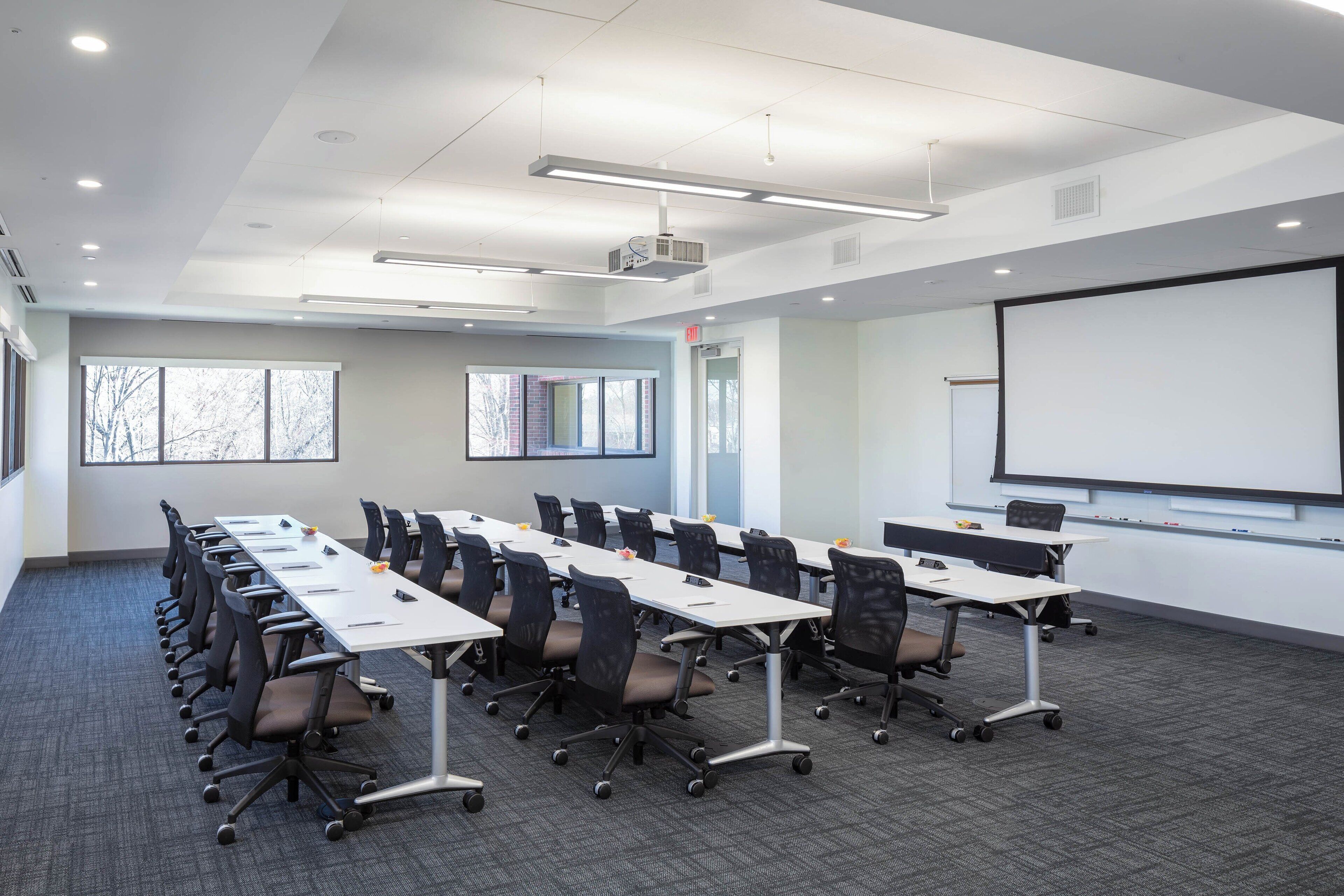 A conference room with a long table, multiple chairs, a projector screen, and a whiteboard.