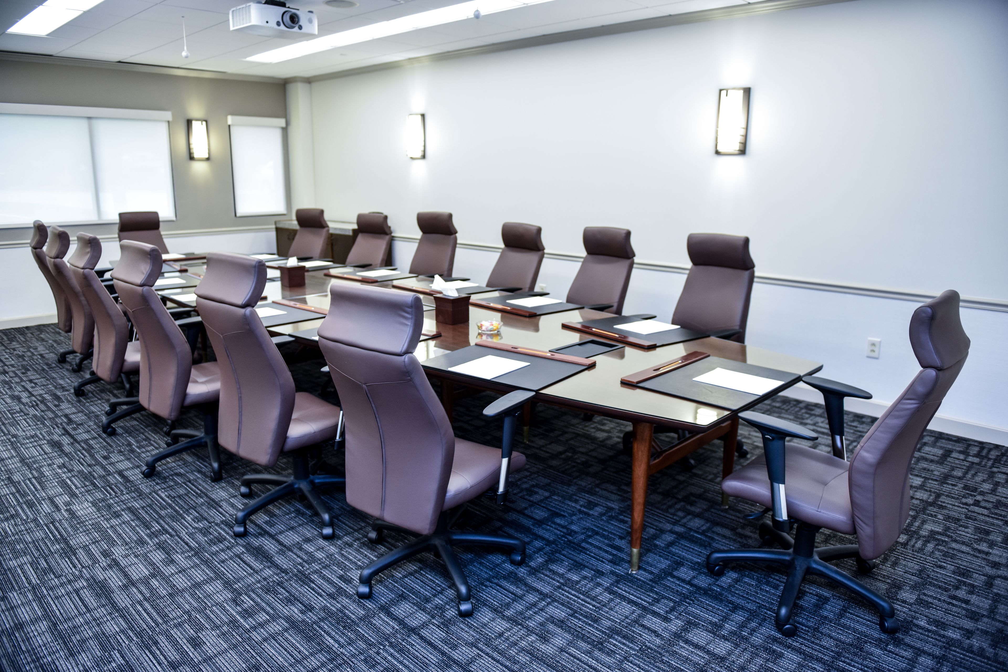 A conference room with a long table, multiple chairs, and a projector screen.