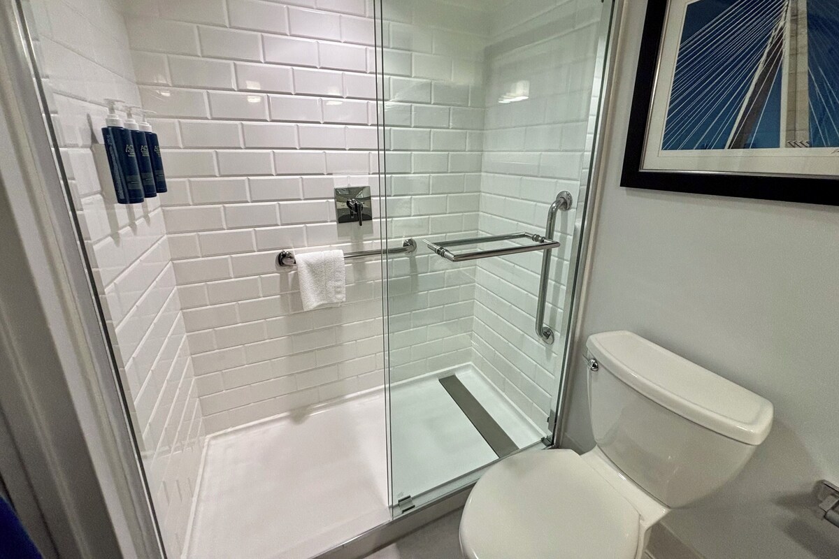 A modern bathroom with a glass-enclosed shower, white tiled walls, a white toilet, and a framed picture on the wall.