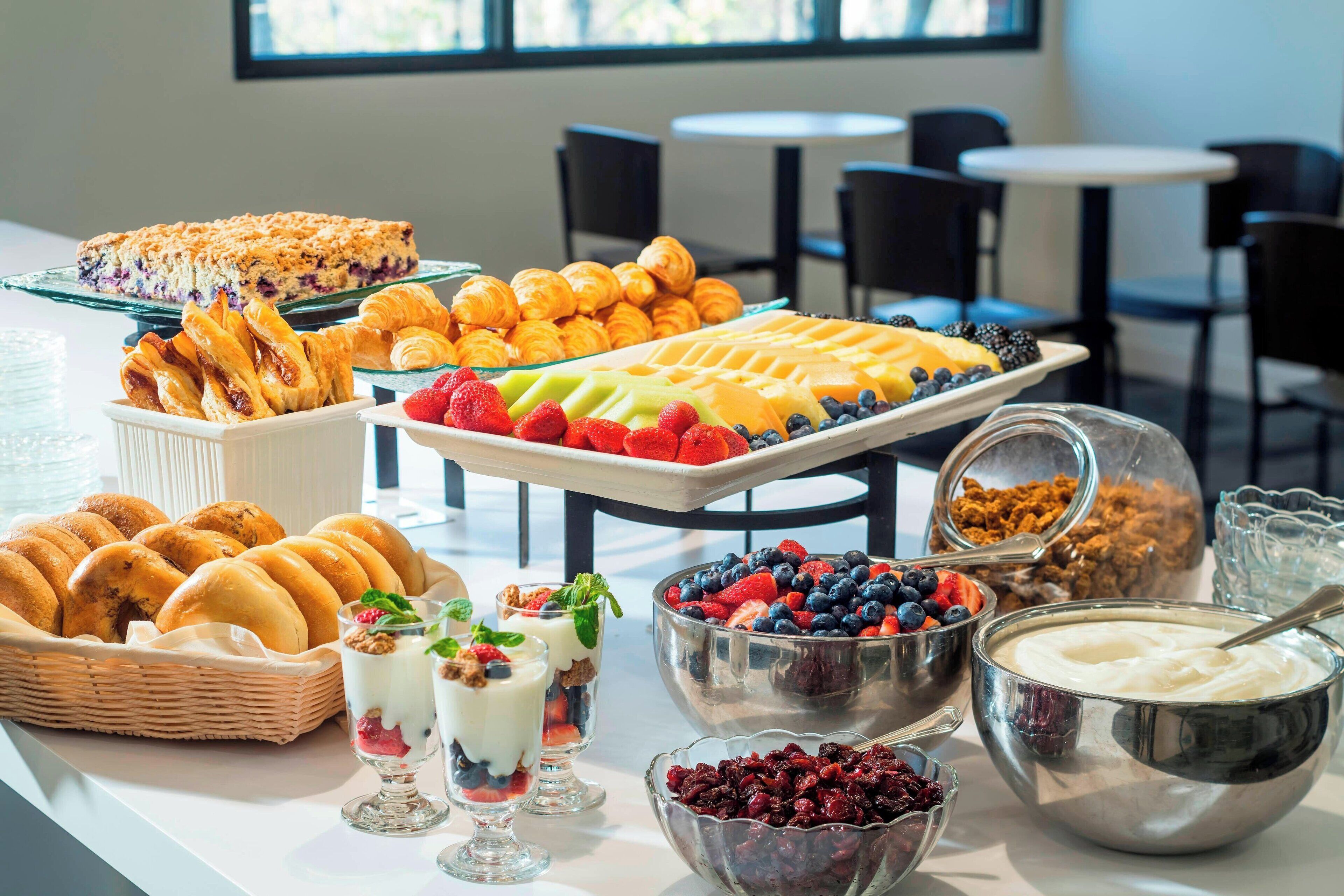 Um buffet de café da manhã com pães, frutas e iogurtes em camadas.